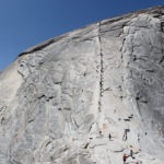 Close up shot of Half Dome with a line of climbers going straight up the middle of the formation on the rope guides.