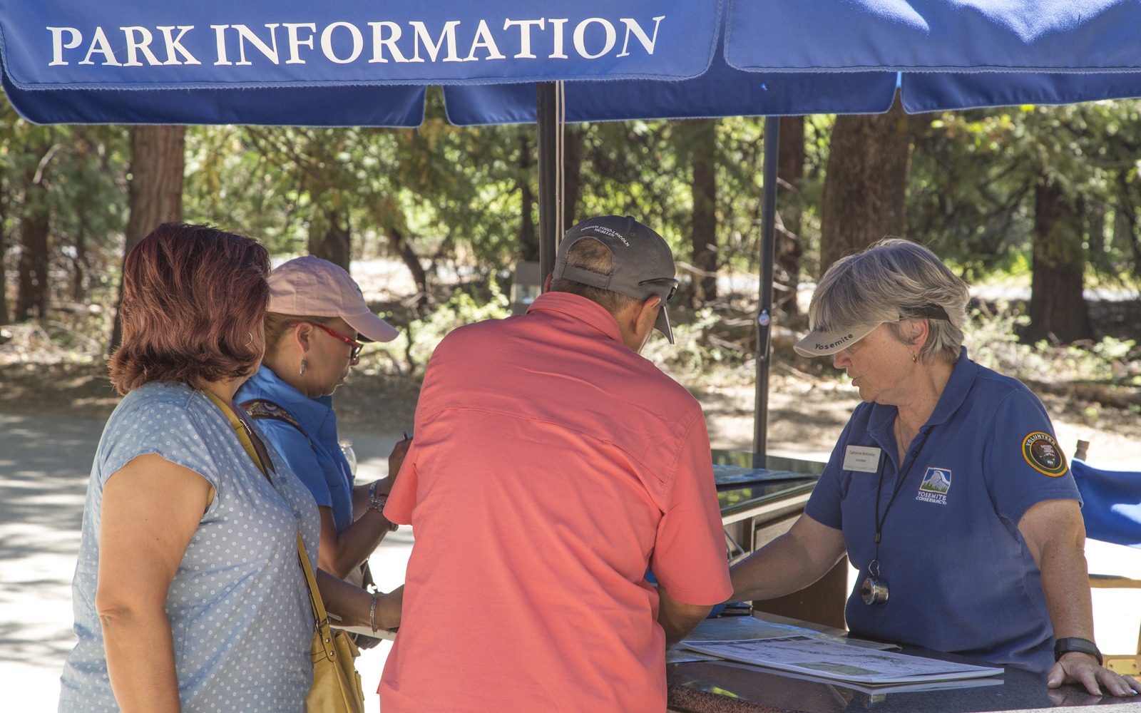 One of our 2019 visitor information assistants talks to visitors at a blue "Park Information" tent near the Yosemite Valley Visitor Center. 