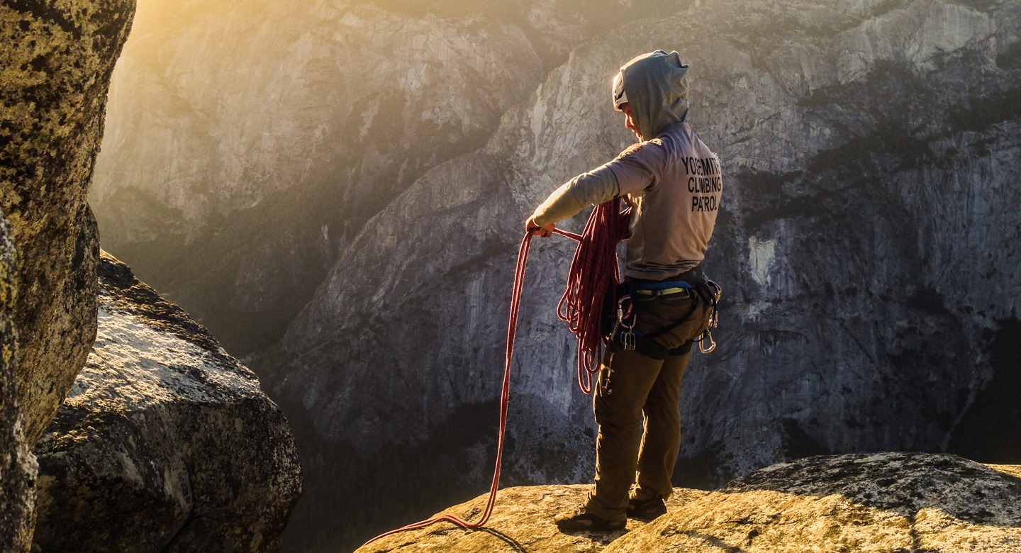 A member of Yosemite's Climbing Patrol stands near Sentinal Rock and wraps climbing cables around their arm.