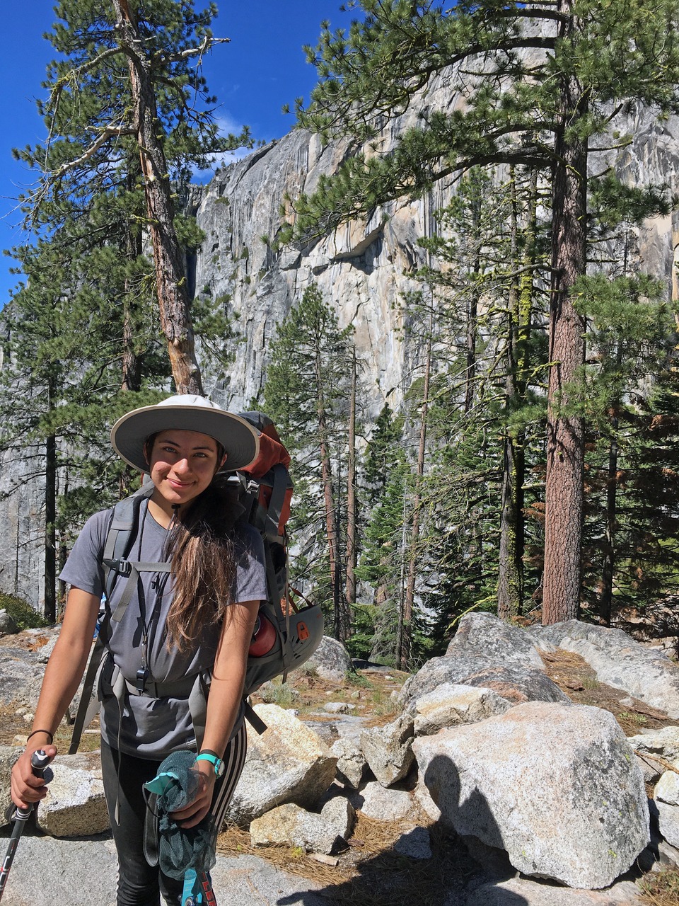 A 2020 Adventure Risk Challenge student smiles for a photo during a backpacking trip in the Yosemite Wilderness, with tall trees and granite in the background. Photo: Courtesy of Adventure Risk Challenge.
