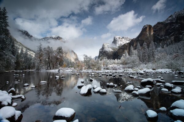 A classic Yosemite in Winter scene: looking up the Merced River filled with snow covered rocks at a foggy El Capitan and Bridalveil Fall. 