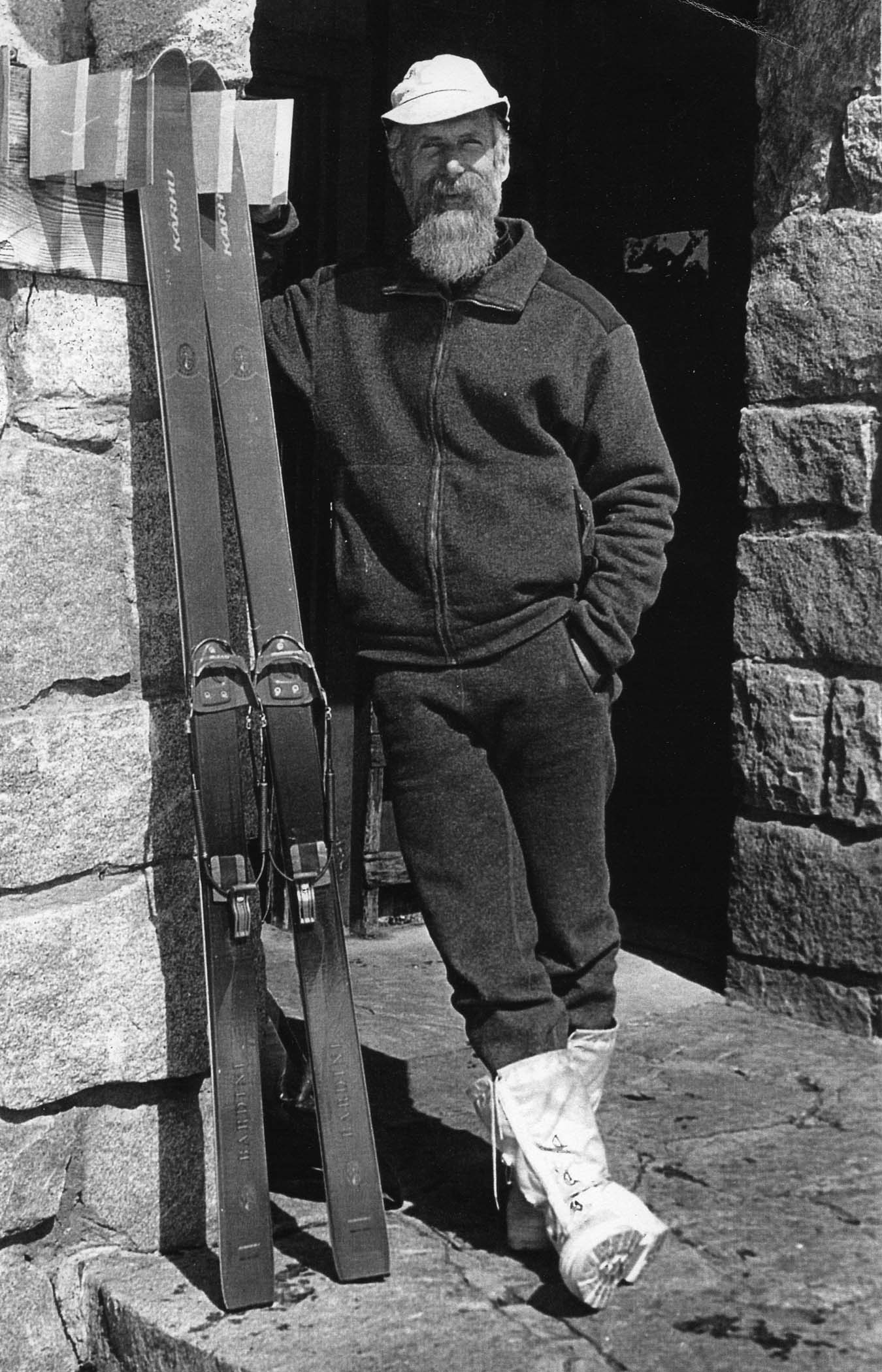 Howard Weamer, the hutkeeper at Ostrander for more than 50 years, leans agains the hut with skis leaning beside him.