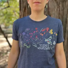 image of someone standing in front of a tree wearing a midnight blue colored tee shirt with colorful drawings of yosemite wildflowers on it