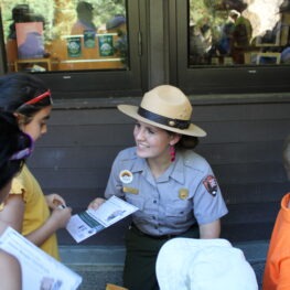 Park ranger handing book to a child as others look on. 