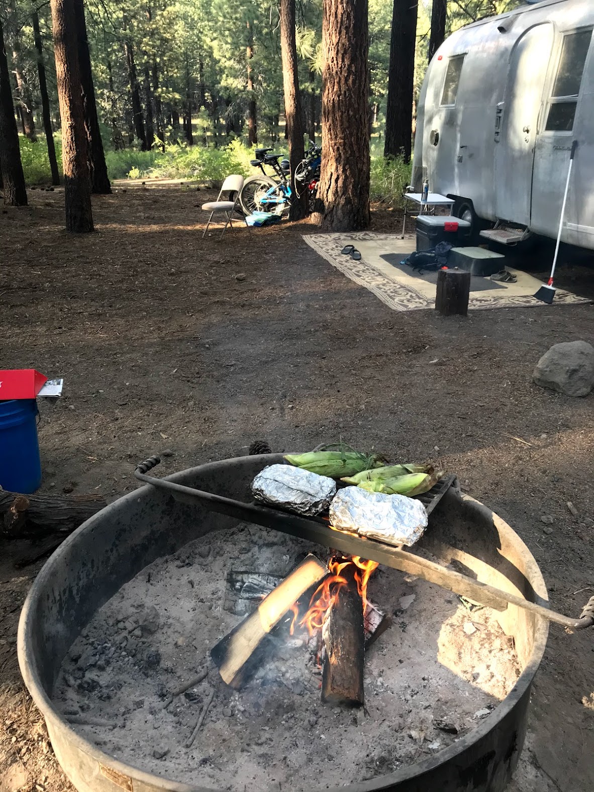 photo of corn and foil wrapped vegetables on the grill over a campfire in a campfire ring