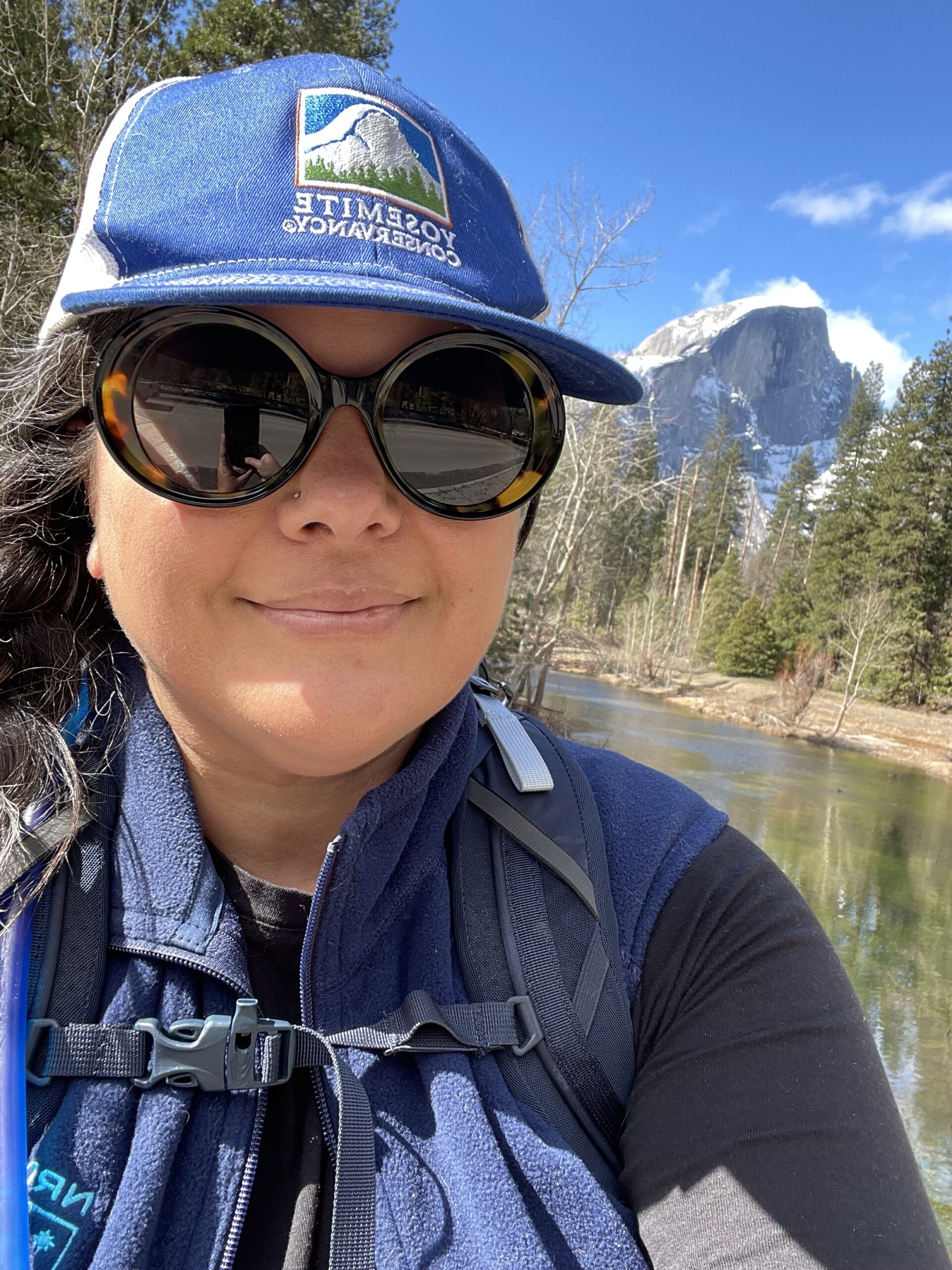 Woman in Yosemite Conservancy ballcap with Yosemite valley and nature behind her 
