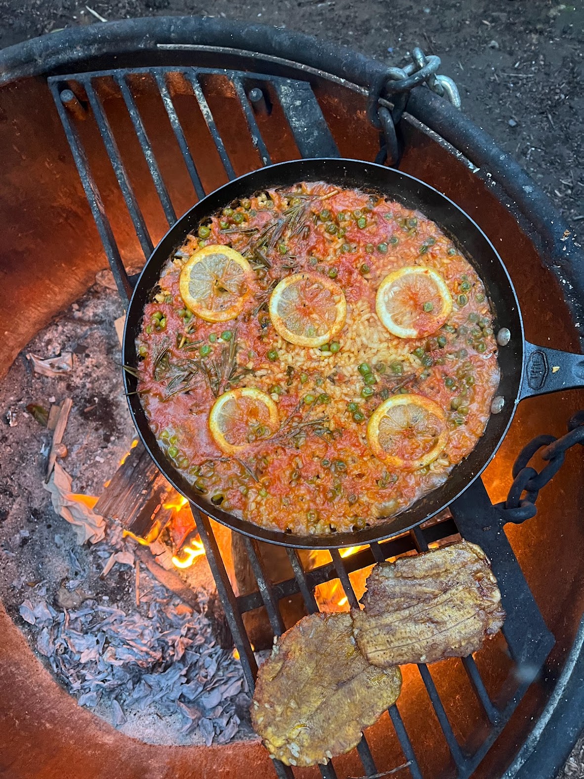 photo of a paella cooking over a camp fire in a fire ring