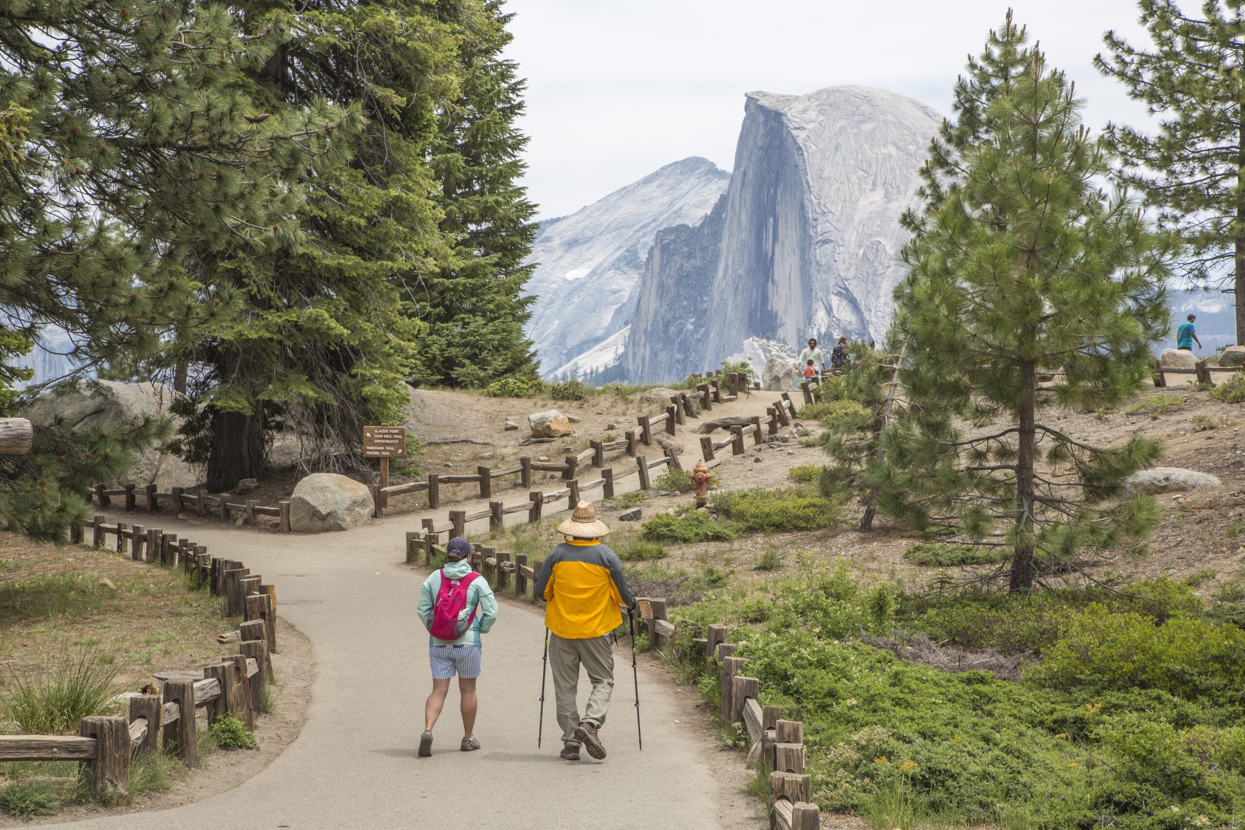 Two people able to access Glacier Point on a flat, paved wide trail. Half Dome is viewable in the distance. 