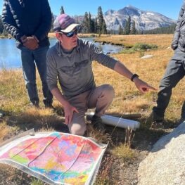Guide with map points at a rock. Visitors look on. 