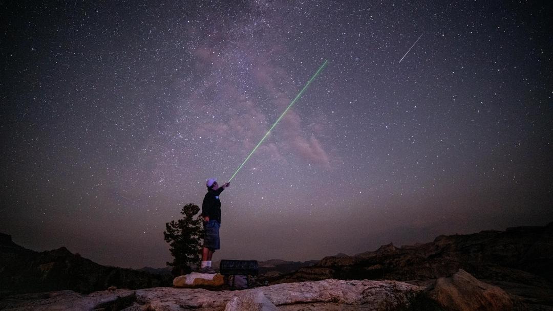 A person points a green laser into the sky filled with stars.