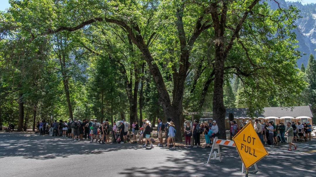 People stand in line near a full Yosemite parking lot.