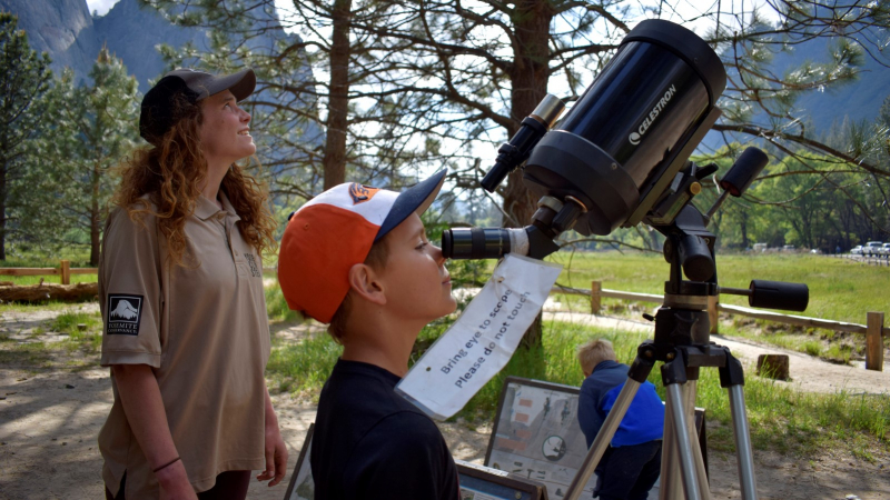 A Yosemite Climber Steward helps a young visitor peer through a telescope at the seasonal Ask a Climber station. Photo: Yosemite Conservancy/Ryan Kelly