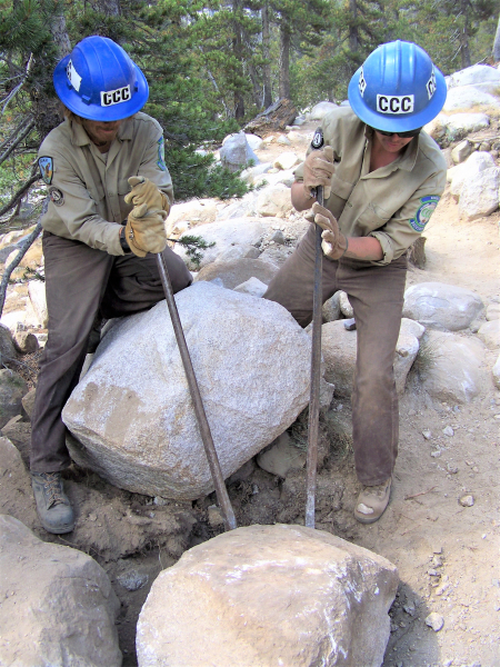 CCC crew members work together to move large rocks on a backcountry trail.